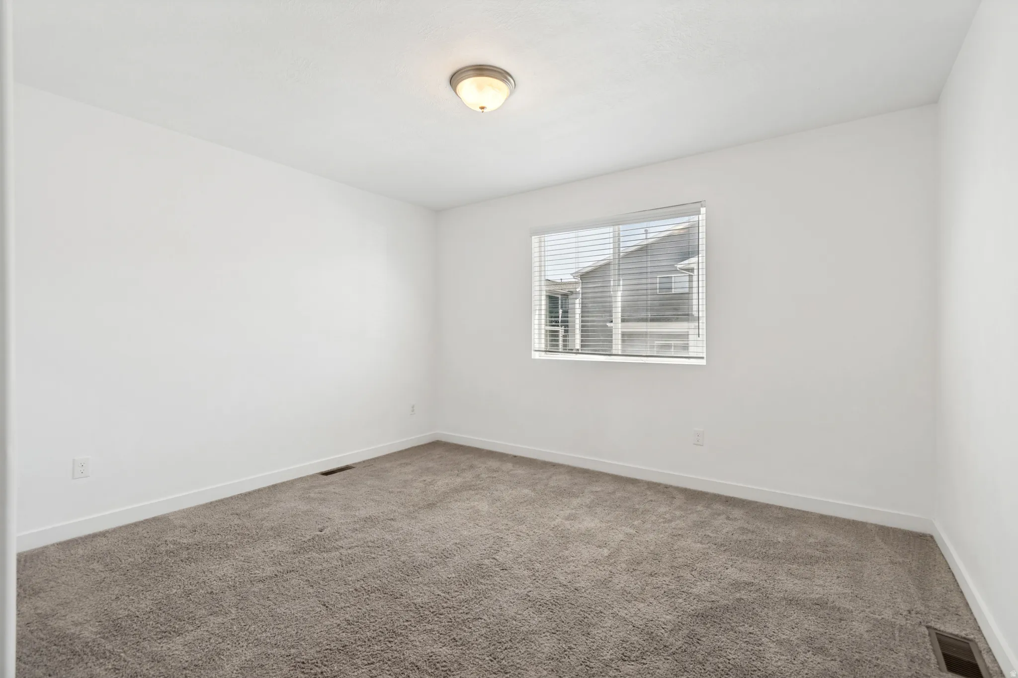 Carpeted room featuring a single window with blinds, white walls, and a ceiling-mounted light fixture