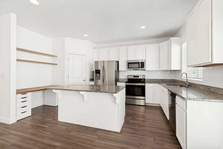 Modern kitchen featuring white cabinetry, granite countertops, subway tile backsplash, and stainless steel appliances