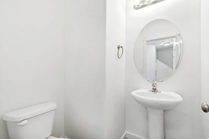 Pedestal sink with an oval frameless mirror and a wall-mounted light fixture