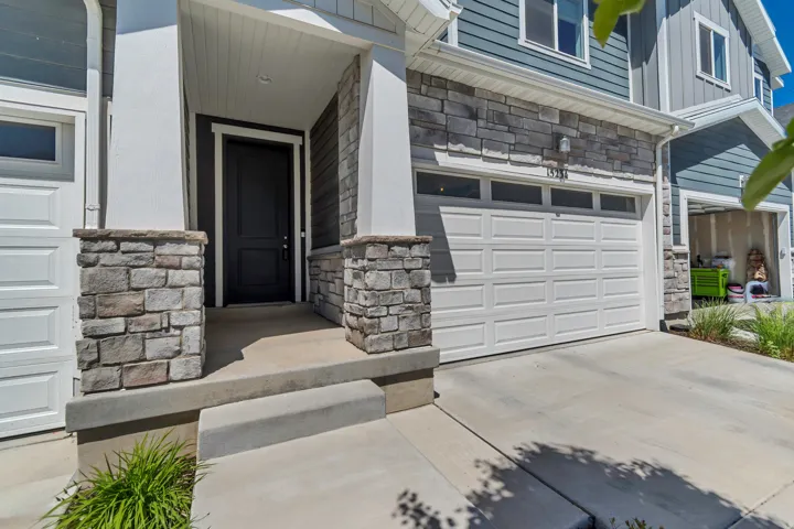 Stone and siding exterior with a dark entry door and a panel-style garage door