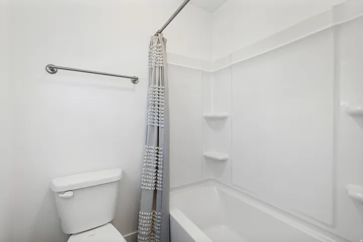 Full-size bathtub with integrated shelving, a white toilet, and a wall-mounted towel bar