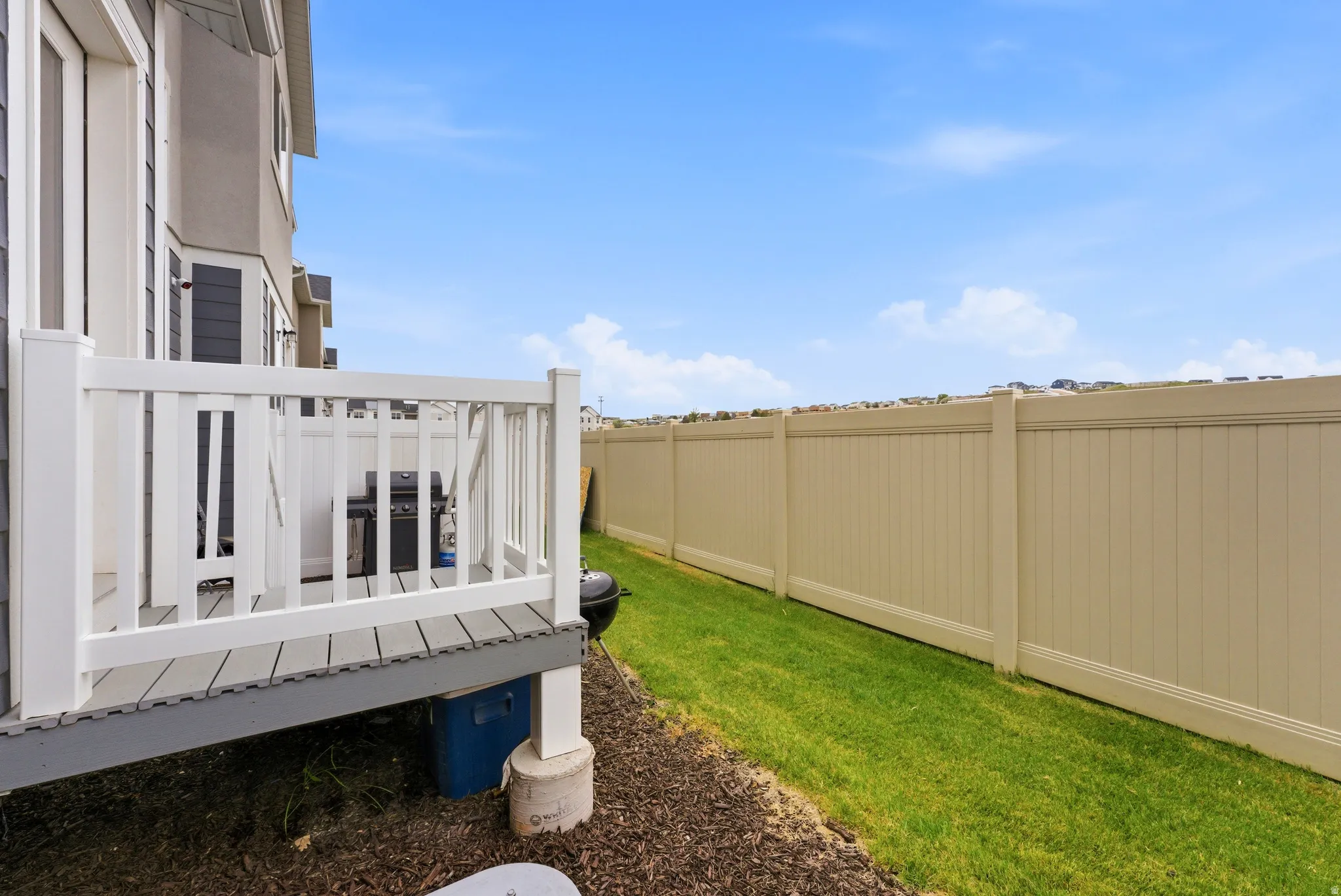 Private outdoor deck with white railing, composite decking, and direct access to a fenced yard with a manicured lawn