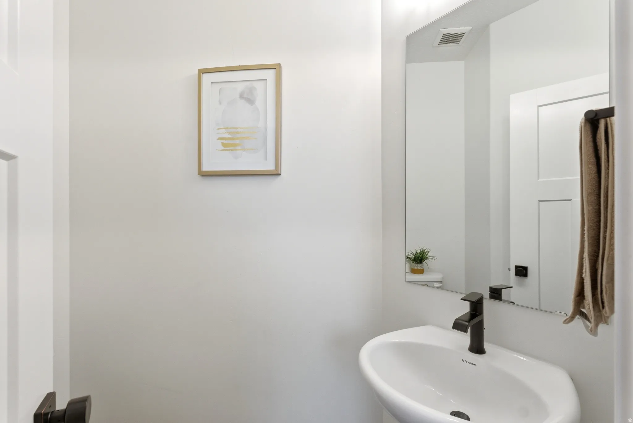 Modern bathroom featuring a wall-mounted sink with a matte black faucet, a large frameless mirror, and neutral wall paint