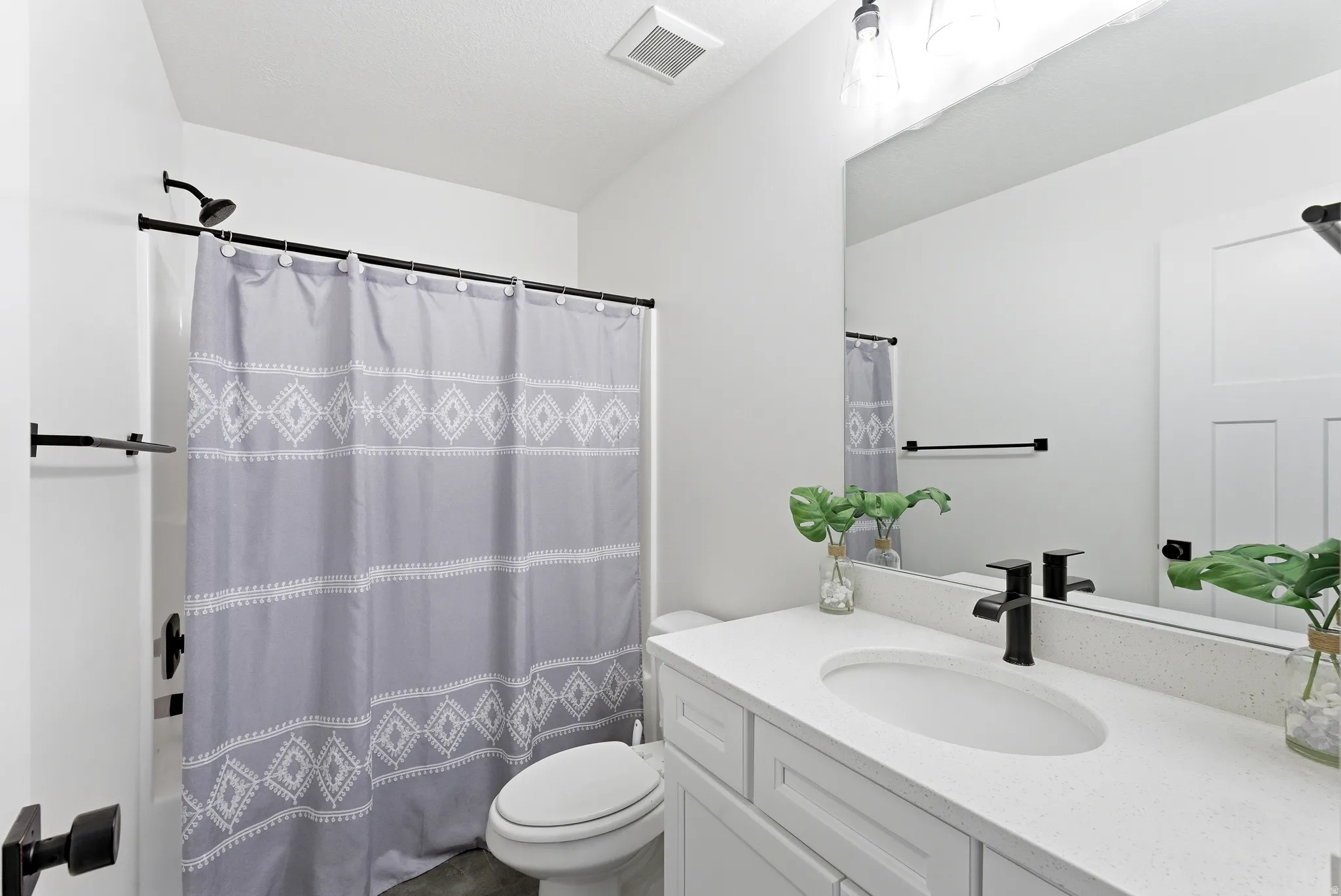 Bathroom featuring a single vanity with an oval undermount sink, a light-colored solid surface countertop, and a matte black single-handle faucet