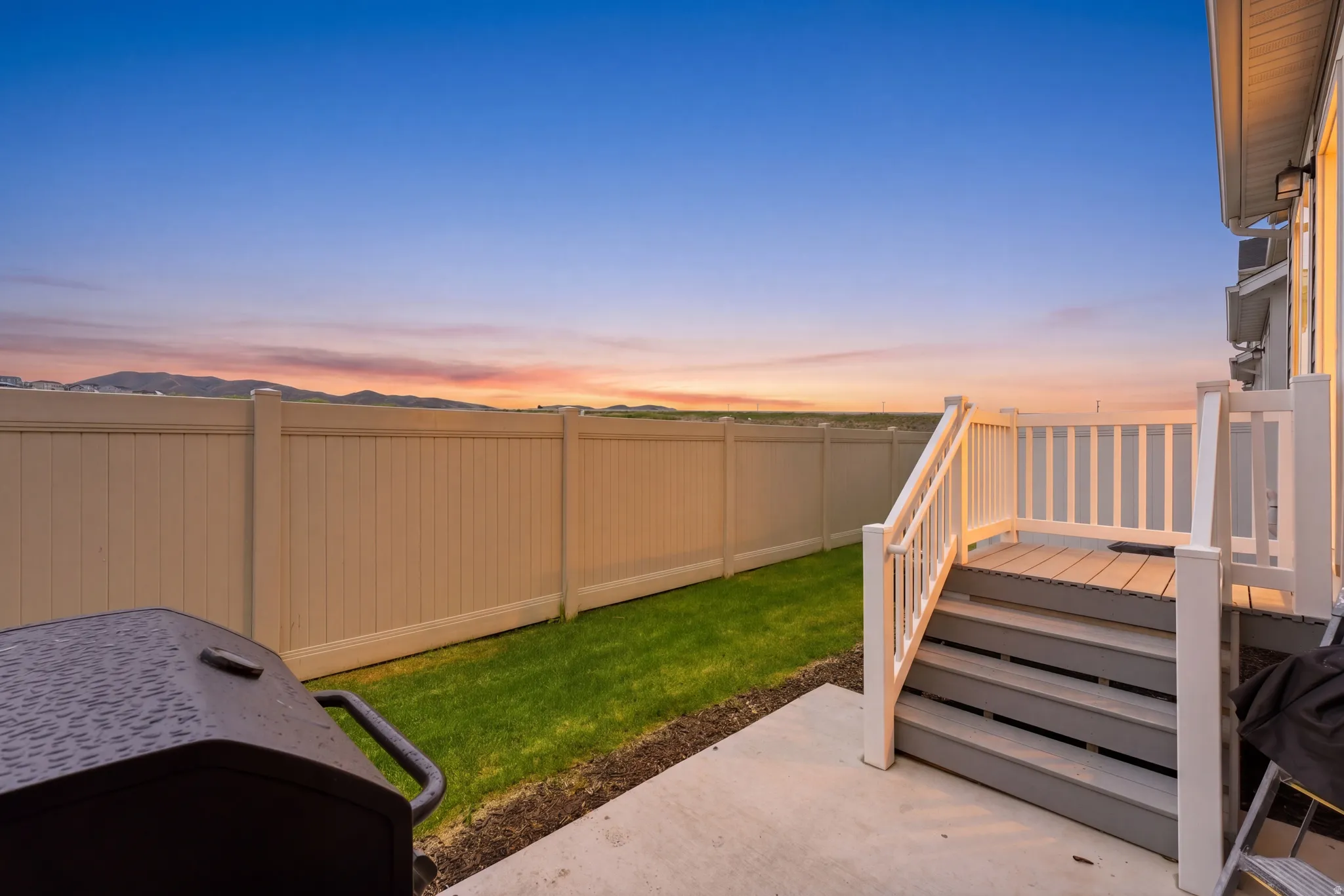 Rear deck with white railings and stairs, a concrete patio, and a fenced yard with a manicured lawn