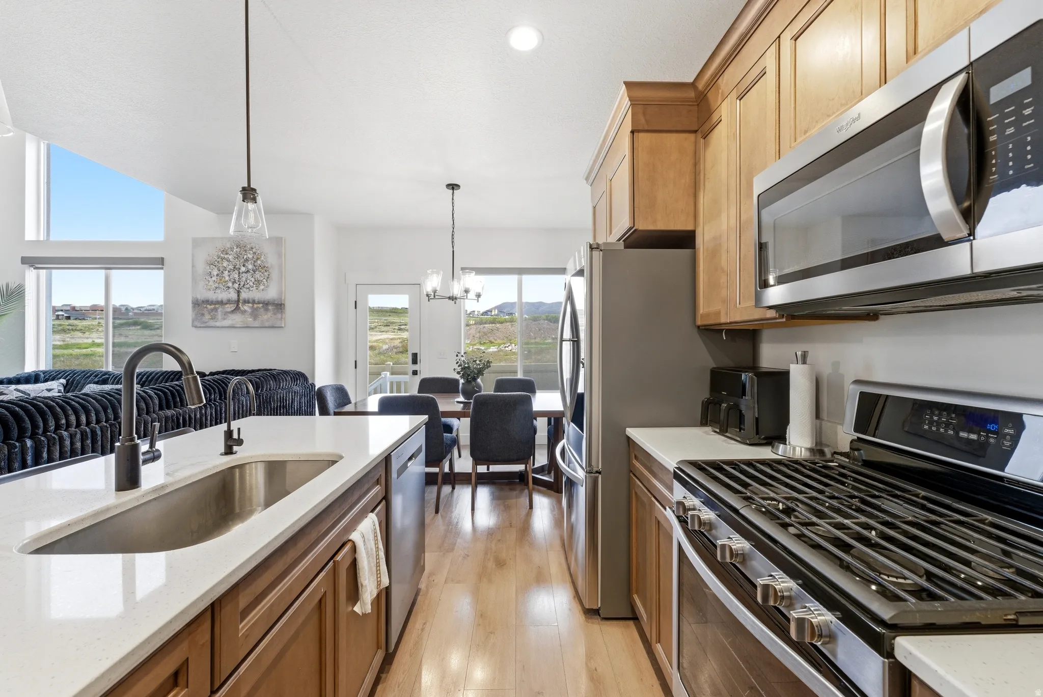Modern kitchen featuring a large island with an undermount sink and dark bronze faucet, stainless steel appliances, wood-finish cabinetry, light countertops, and wood-finish flooring
