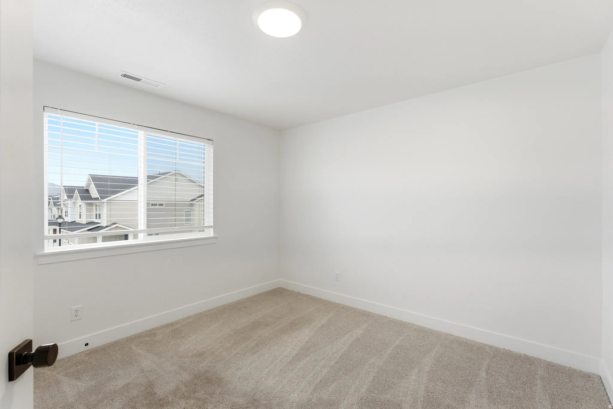 Room featuring neutral-toned carpeting, white walls, and a large window with blinds