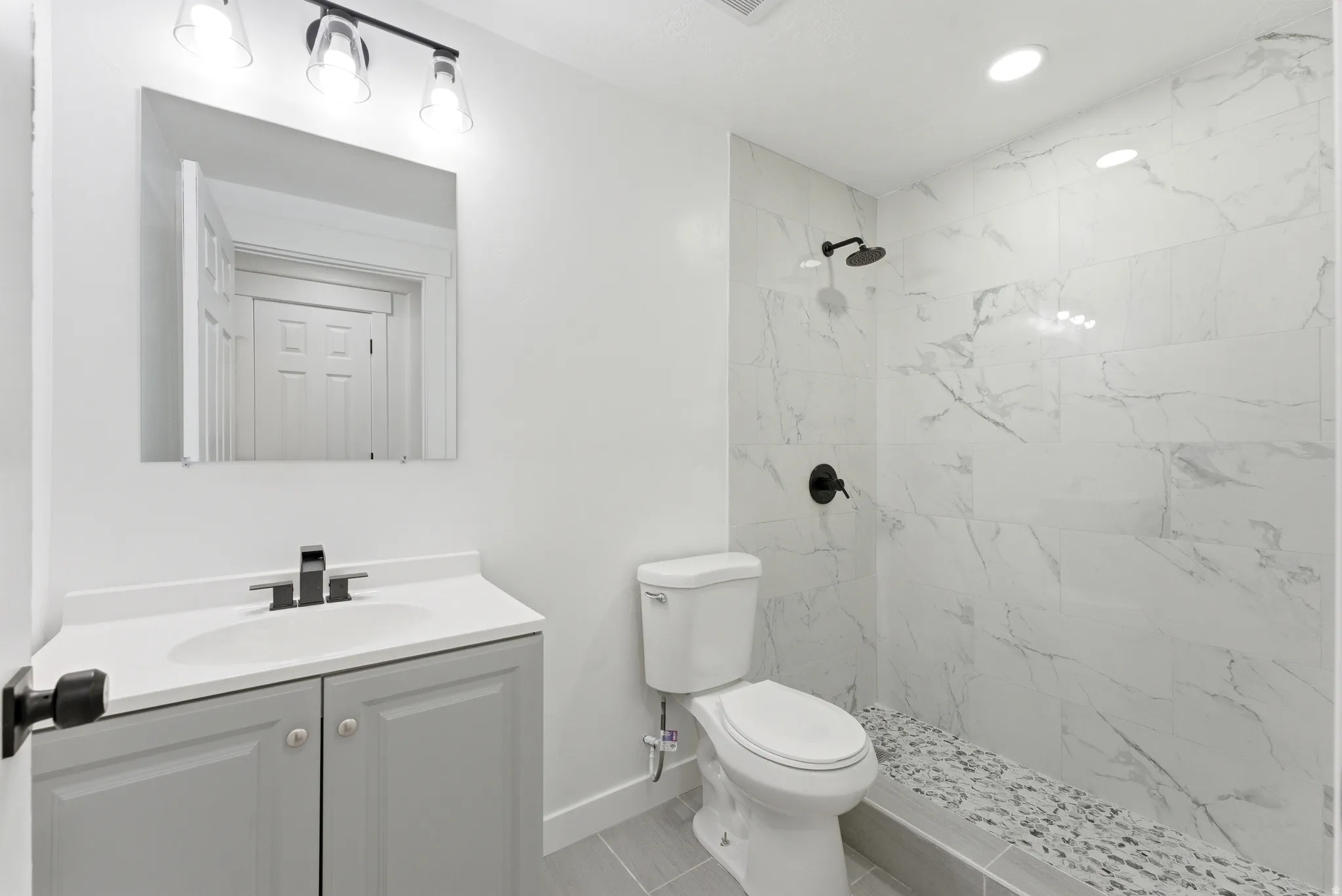 Bathroom featuring a tiled shower with a pebble floor, a wall-mounted shower head, and matte black fixtures