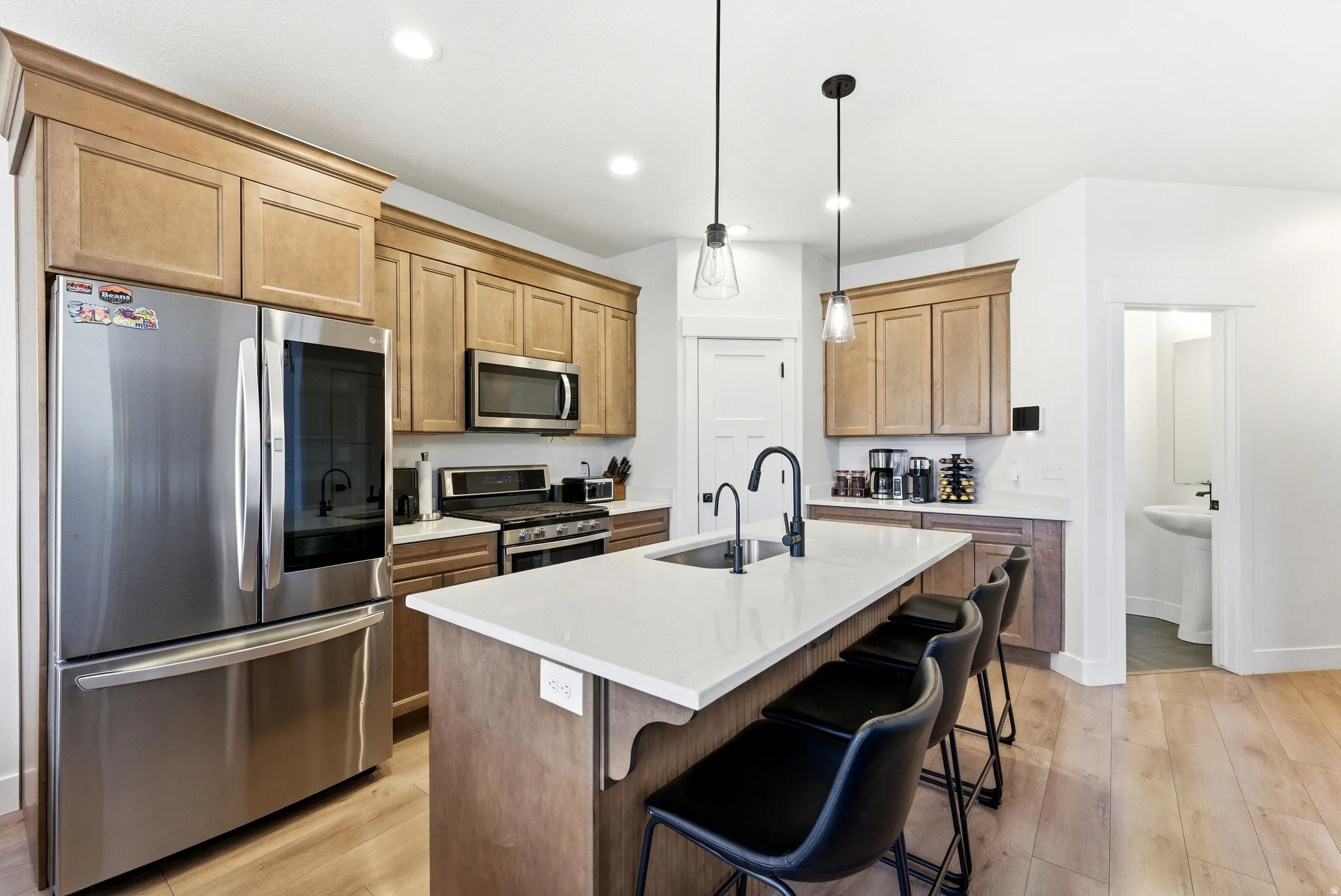 Spacious kitchen featuring an extended island with seating, stainless steel appliances, wood-finish flooring, recessed lighting, and pendant lighting fixtures