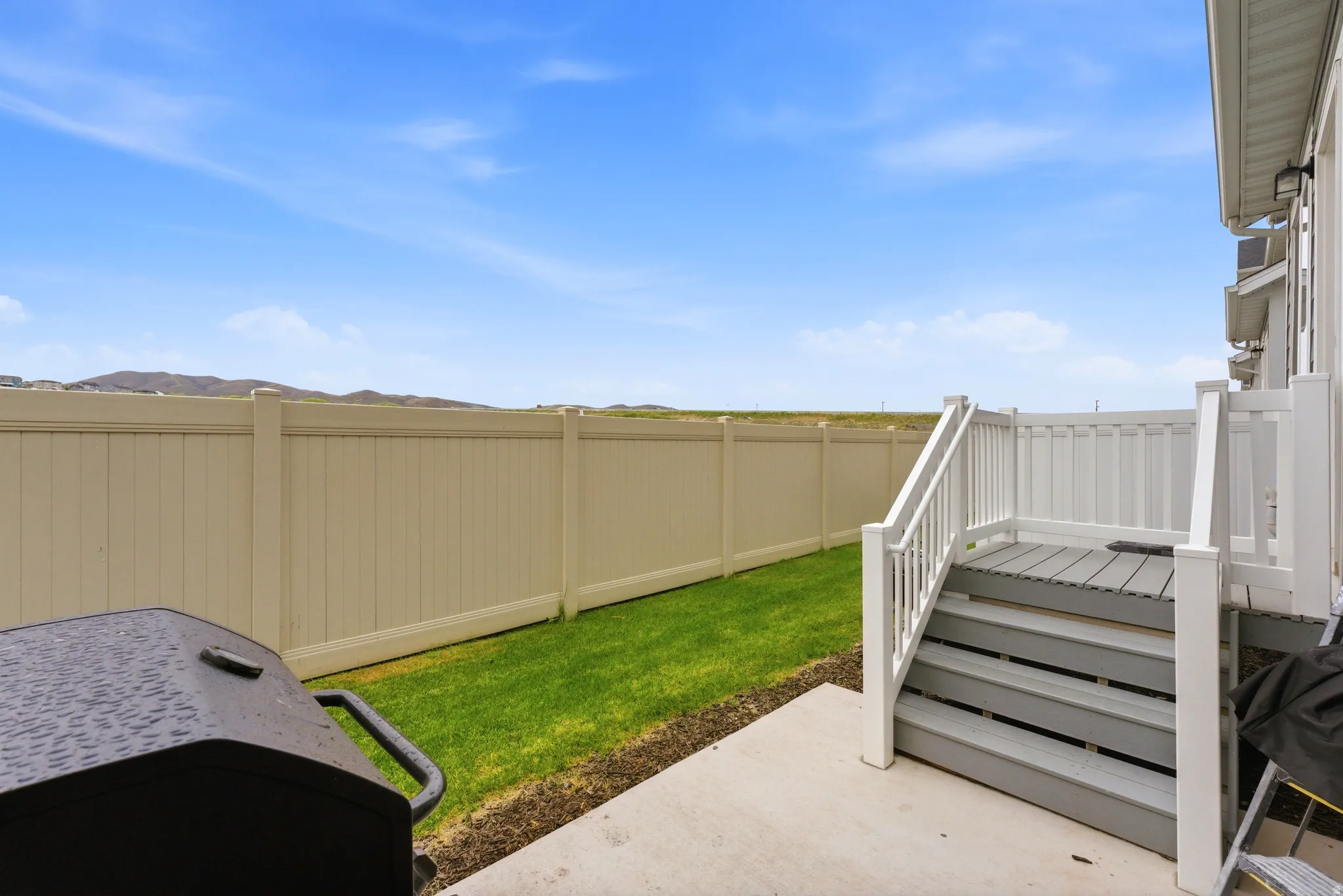 Private backyard featuring a concrete patio, green lawn, and a light-colored privacy fence