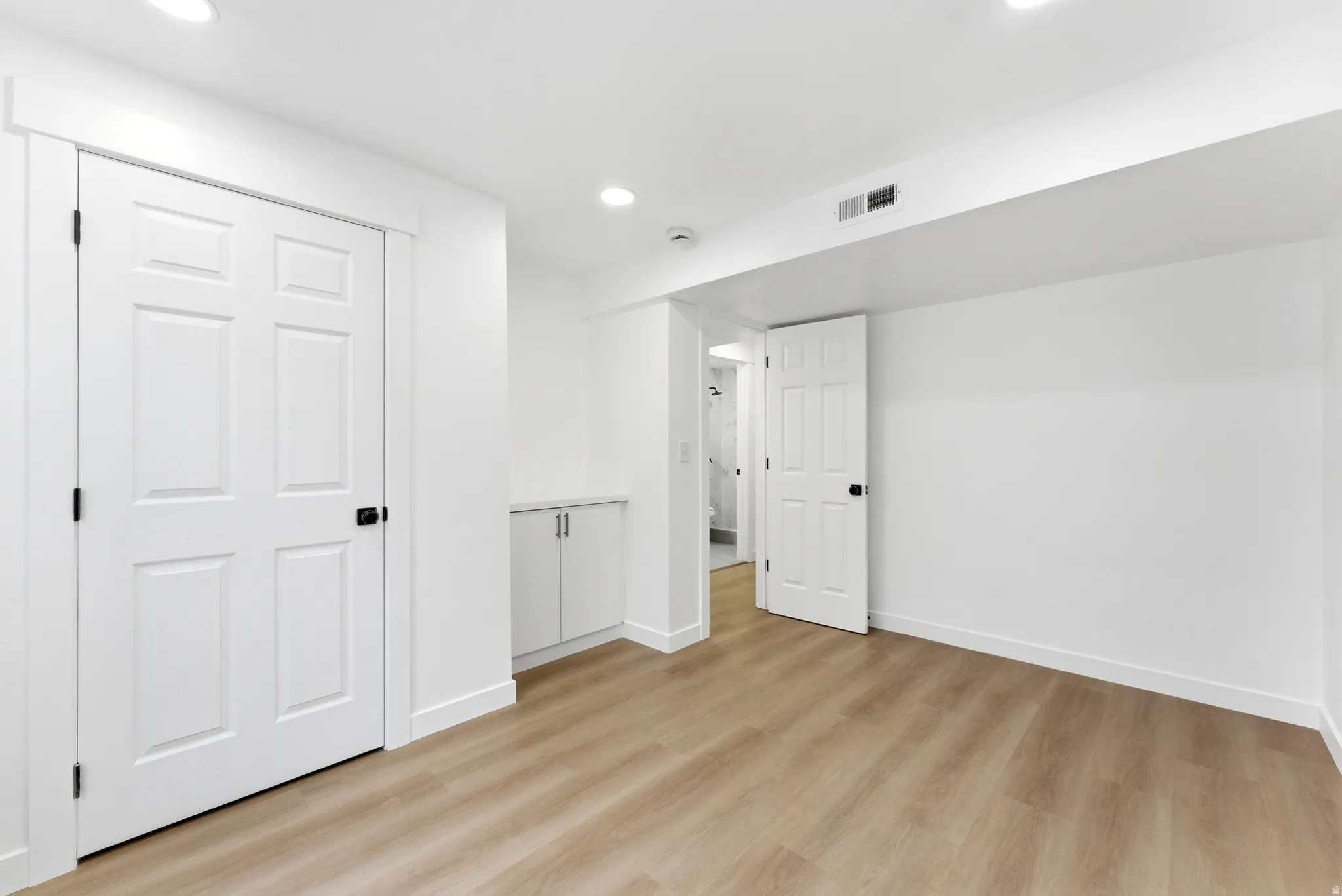 Spacious room featuring wood-finish flooring, recessed lighting, and bright white walls