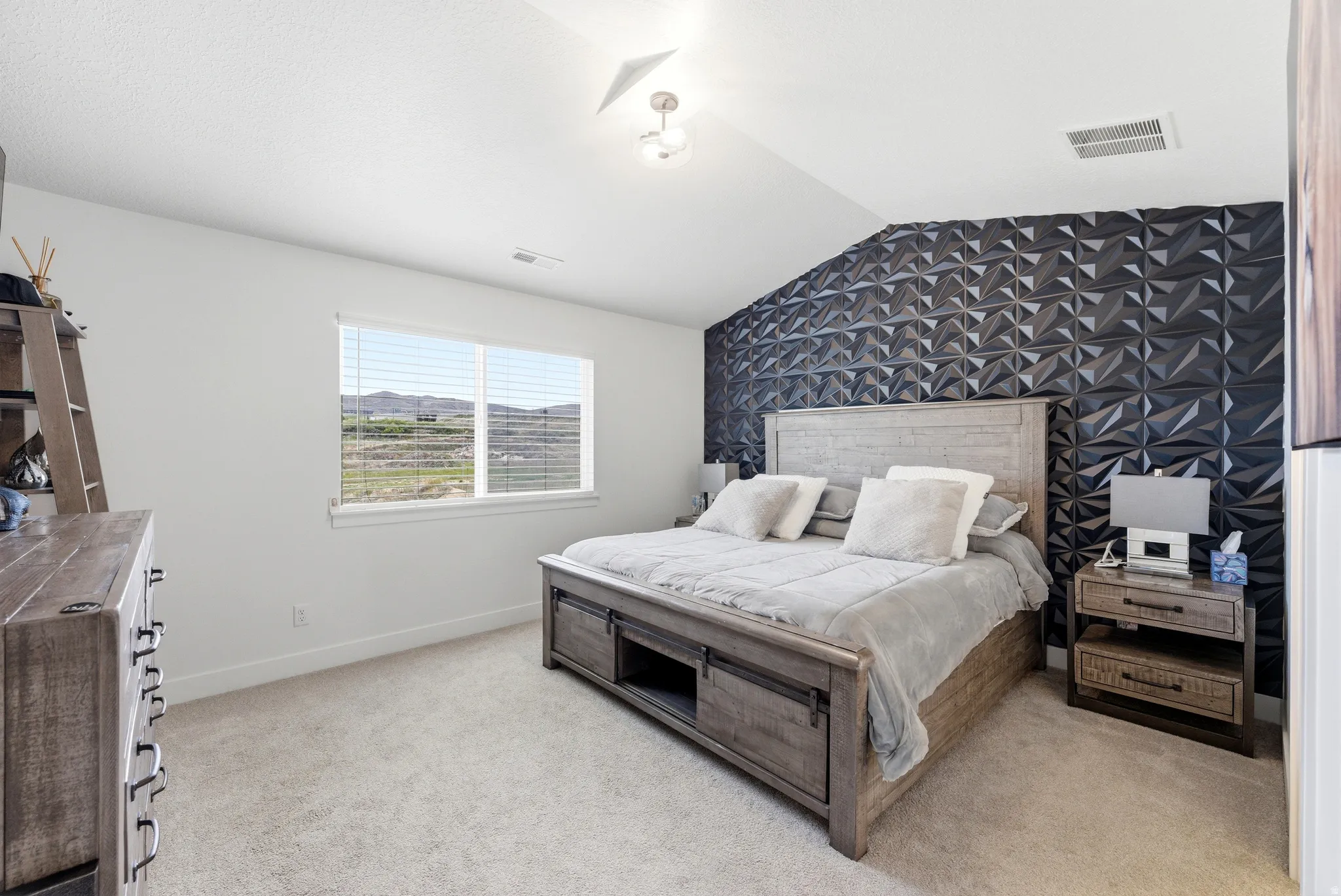 Accent wall featuring geometric paneling, vaulted ceiling with a flush mount light fixture, textured carpeting, and a window with horizontal blinds