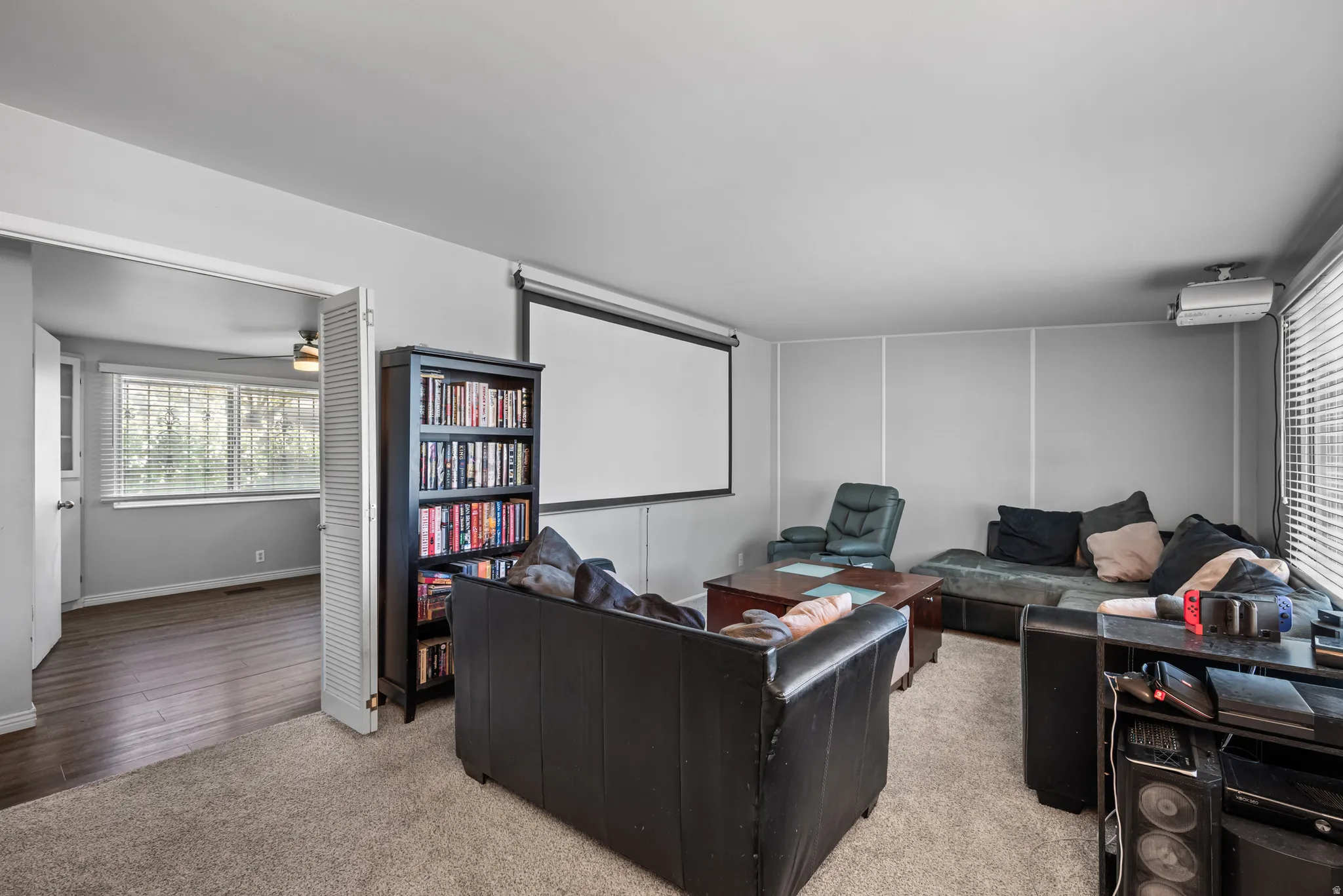 Entertainment room featuring a wall-mounted projector screen, light gray walls, and textured carpeting