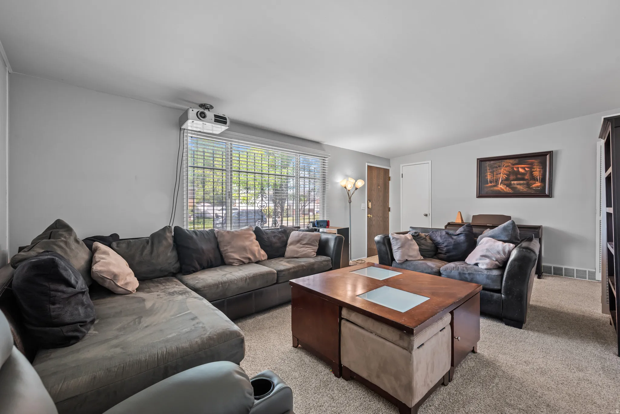 Living area featuring light gray walls, textured carpet flooring, and a front entry door with a sidelight