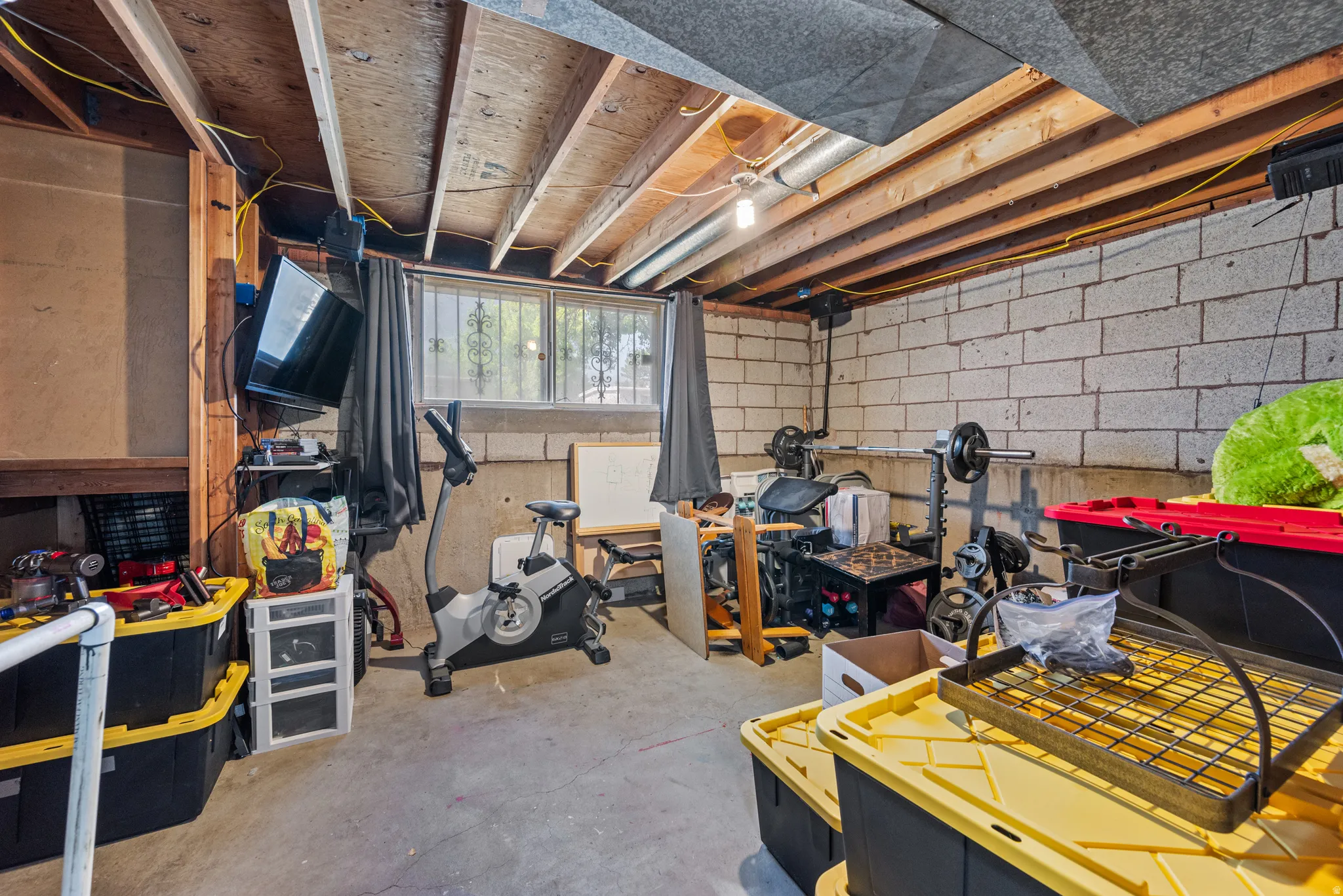 Unfinished basement featuring exposed wood ceiling joists, concrete block walls, a concrete floor, and a window with security bars