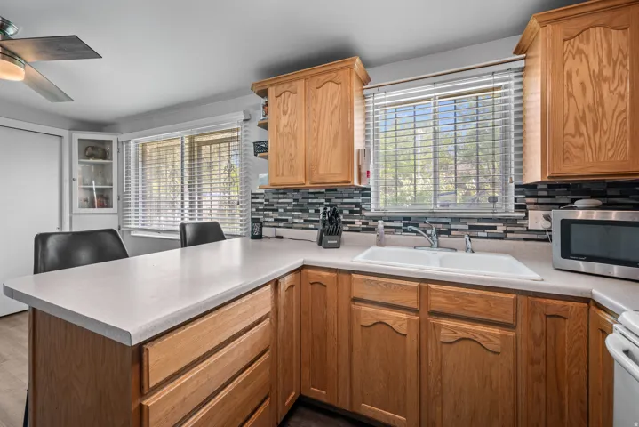 Kitchen featuring wood cabinetry, light-toned countertops, a mosaic tile backsplash, and a double basin sink