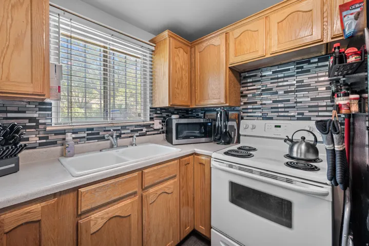 Kitchen featuring wood cabinetry, a dual basin sink, a mosaic tile backsplash, and a white electric range