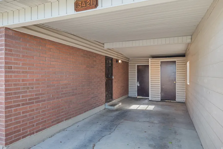 Carport featuring a red brick wall, two built-in storage units, and a concrete floor