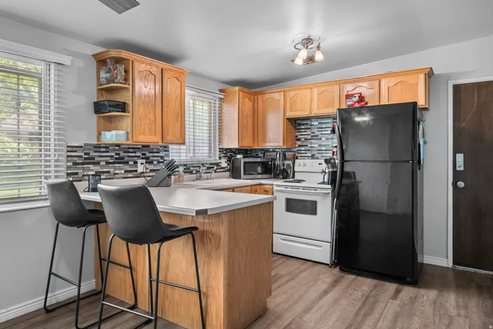 Kitchen featuring wood-finish cabinetry, a white countertop island with bar seating, and a mosaic tile backsplash