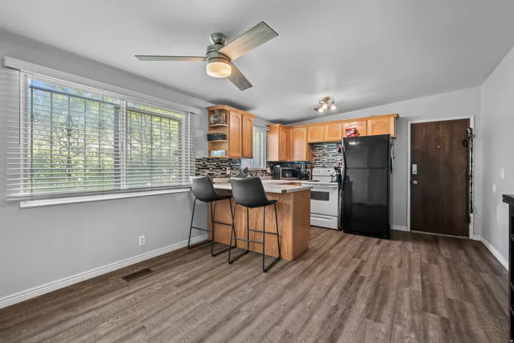 Kitchen and dining area featuring wood-finish flooring, light wood cabinetry, white appliances, and a mosaic tile backsplash