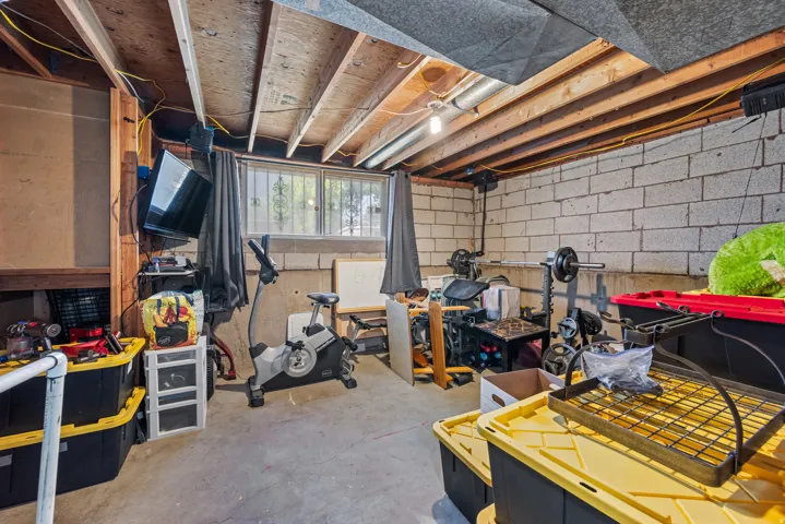 Unfinished basement featuring exposed wood ceiling joists, concrete block walls, a concrete floor, and a window with security bars