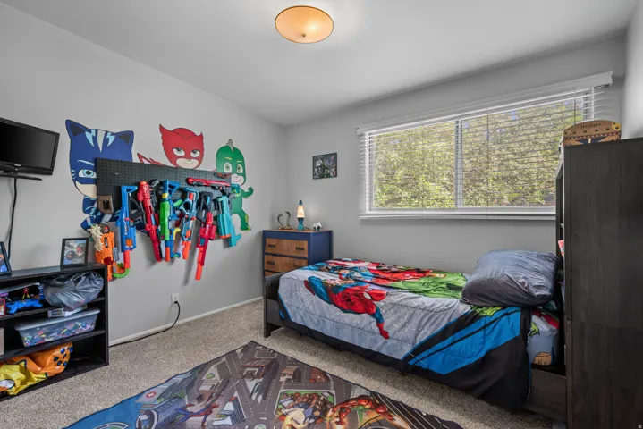 Bedroom featuring light gray walls, plush carpeting, a large window with white blinds, and a flush-mount ceiling light fixture