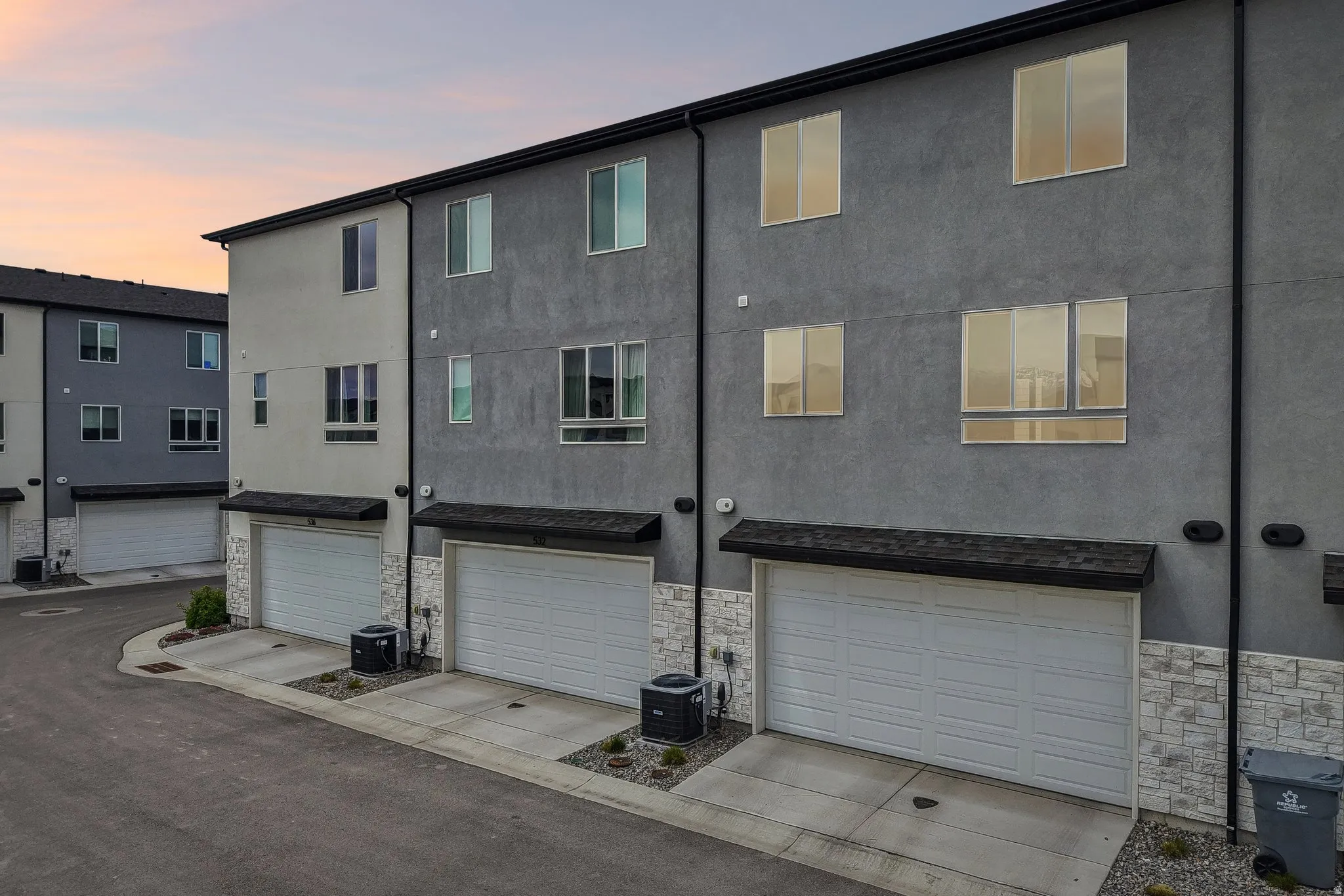 Back of property at dusk with stone siding, an attached garage, stucco siding, and concrete driveway