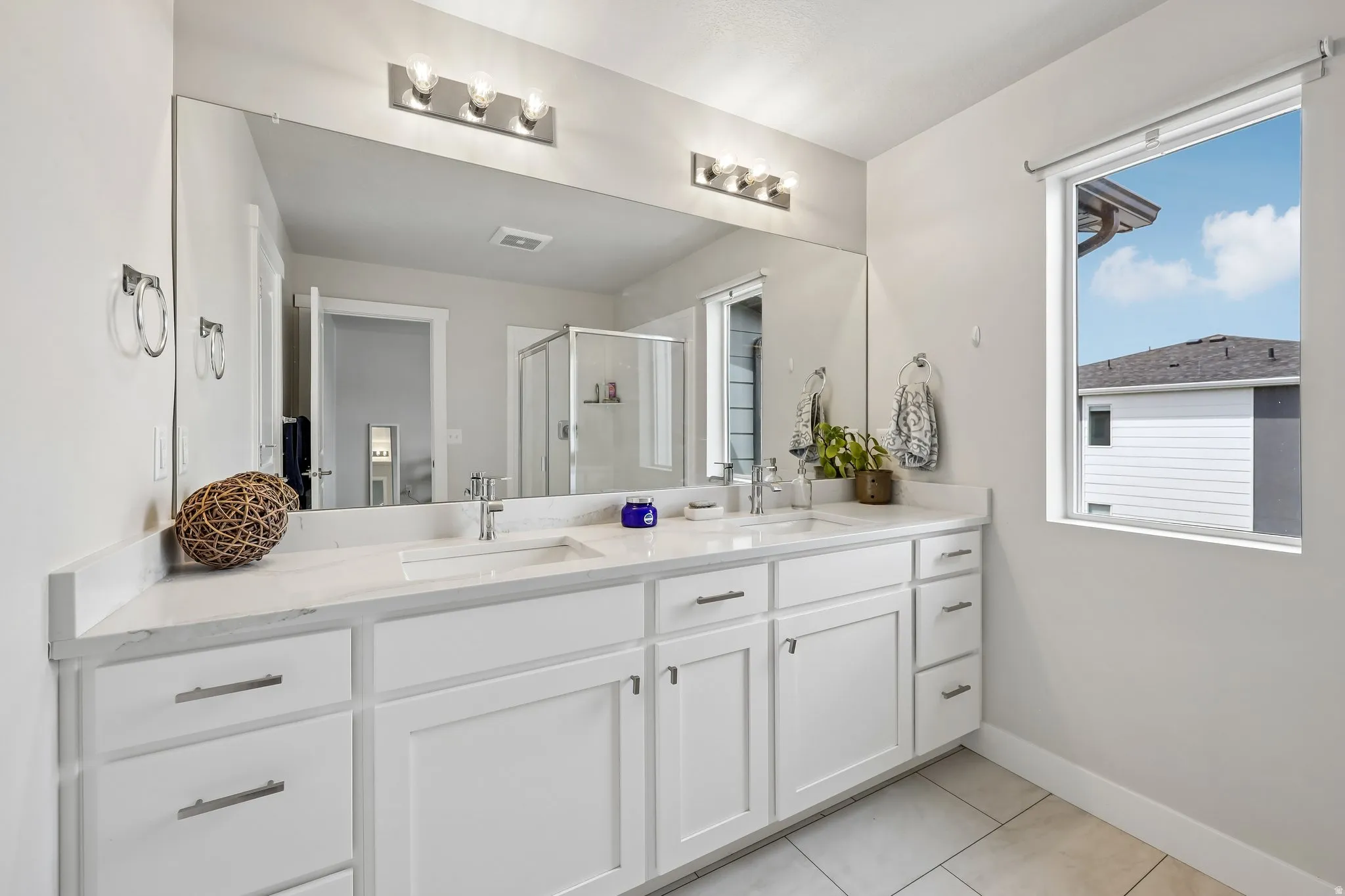 Full bath featuring double vanity, a stall shower, and light tile patterned flooring