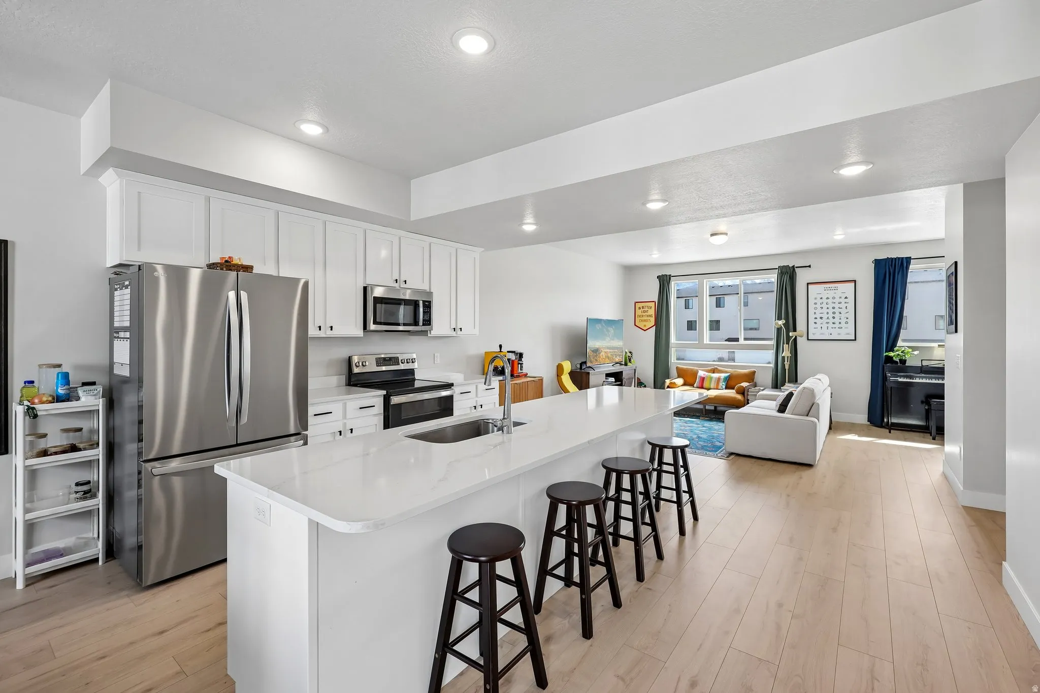 Kitchen featuring stainless steel appliances, white cabinetry, a breakfast bar, light wood-type flooring, and recessed lighting