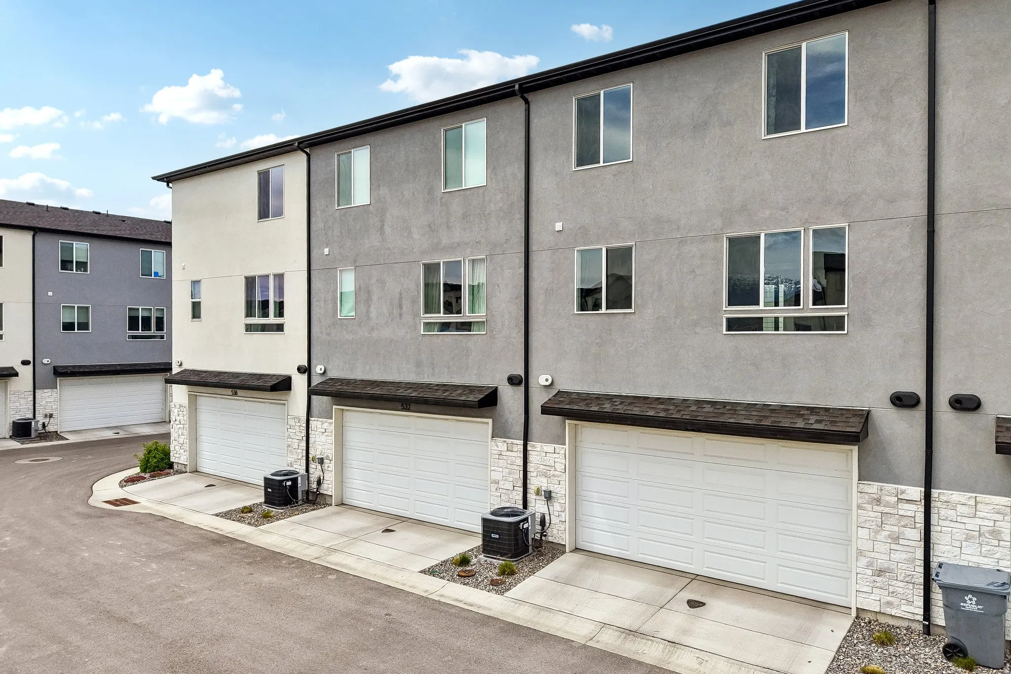 Back of property with stucco siding, an attached garage, stone siding, and driveway
