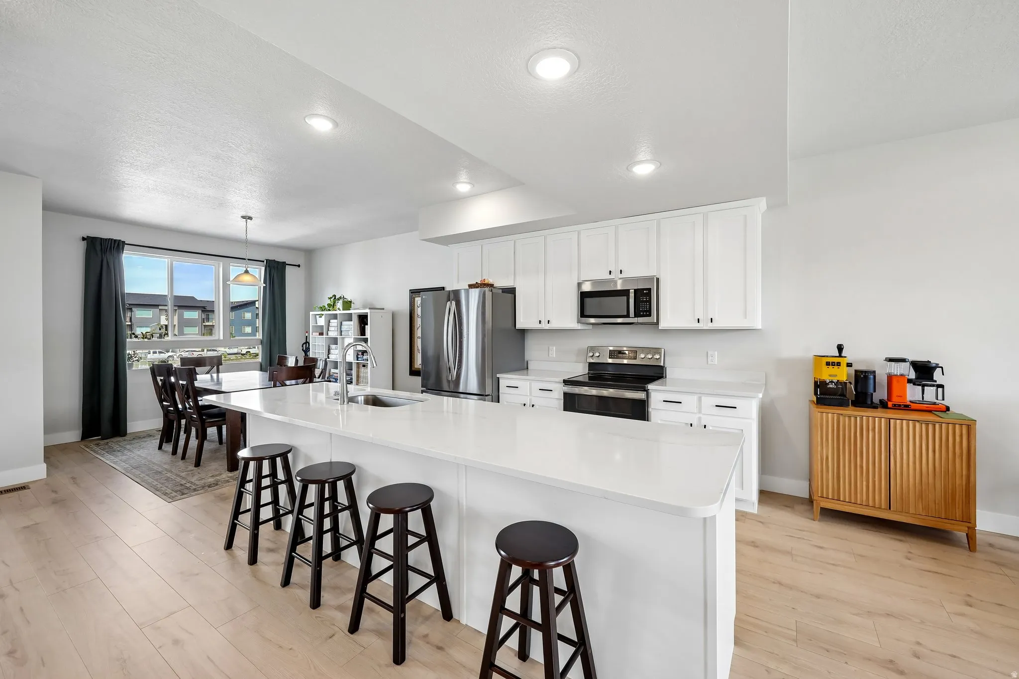Kitchen featuring a kitchen bar, light wood-style floors, stainless steel appliances, white cabinetry, and a textured ceiling