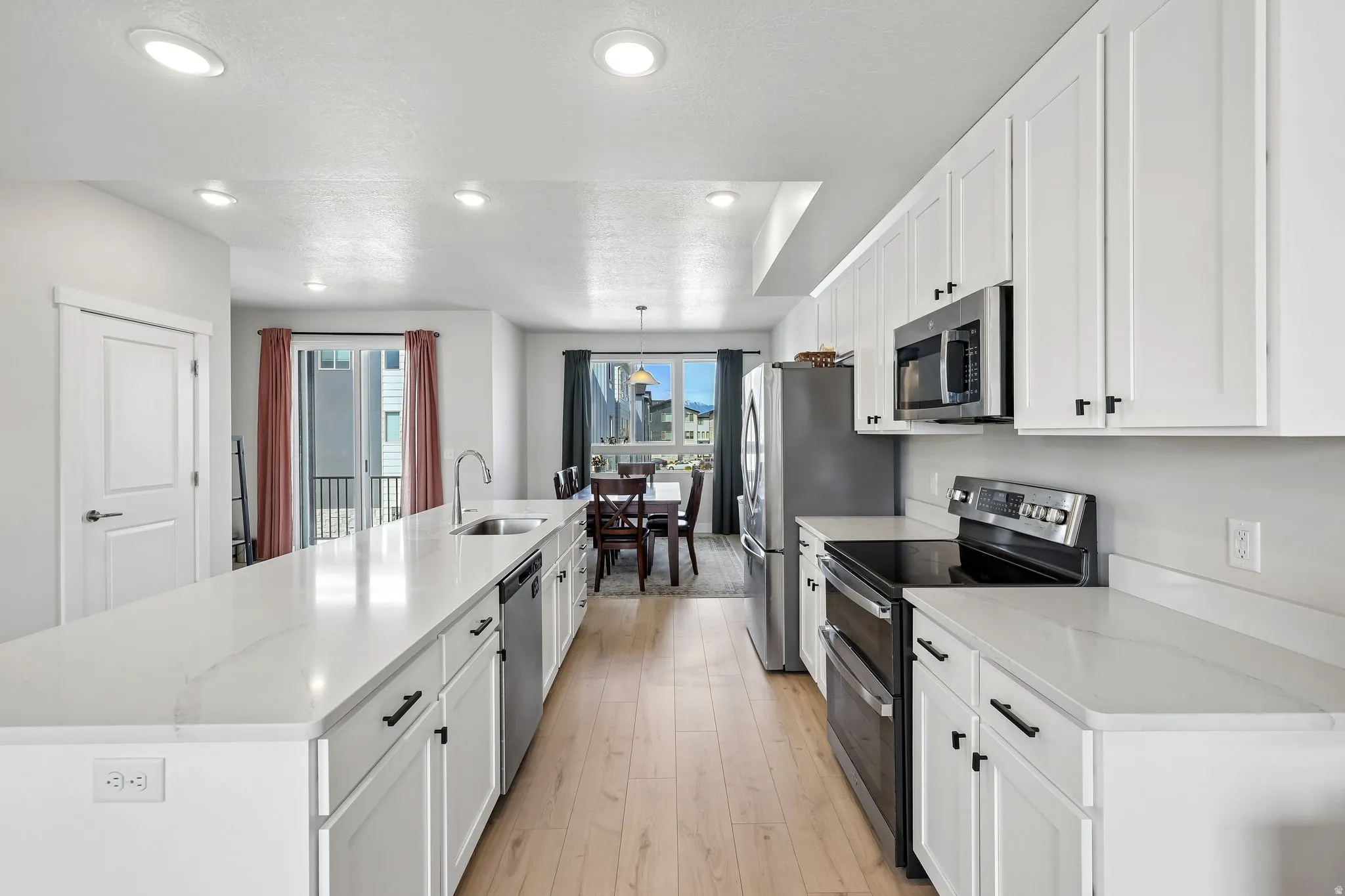 Kitchen with a large island, stainless steel appliances, white cabinets, light wood finished floors, and light stone countertops