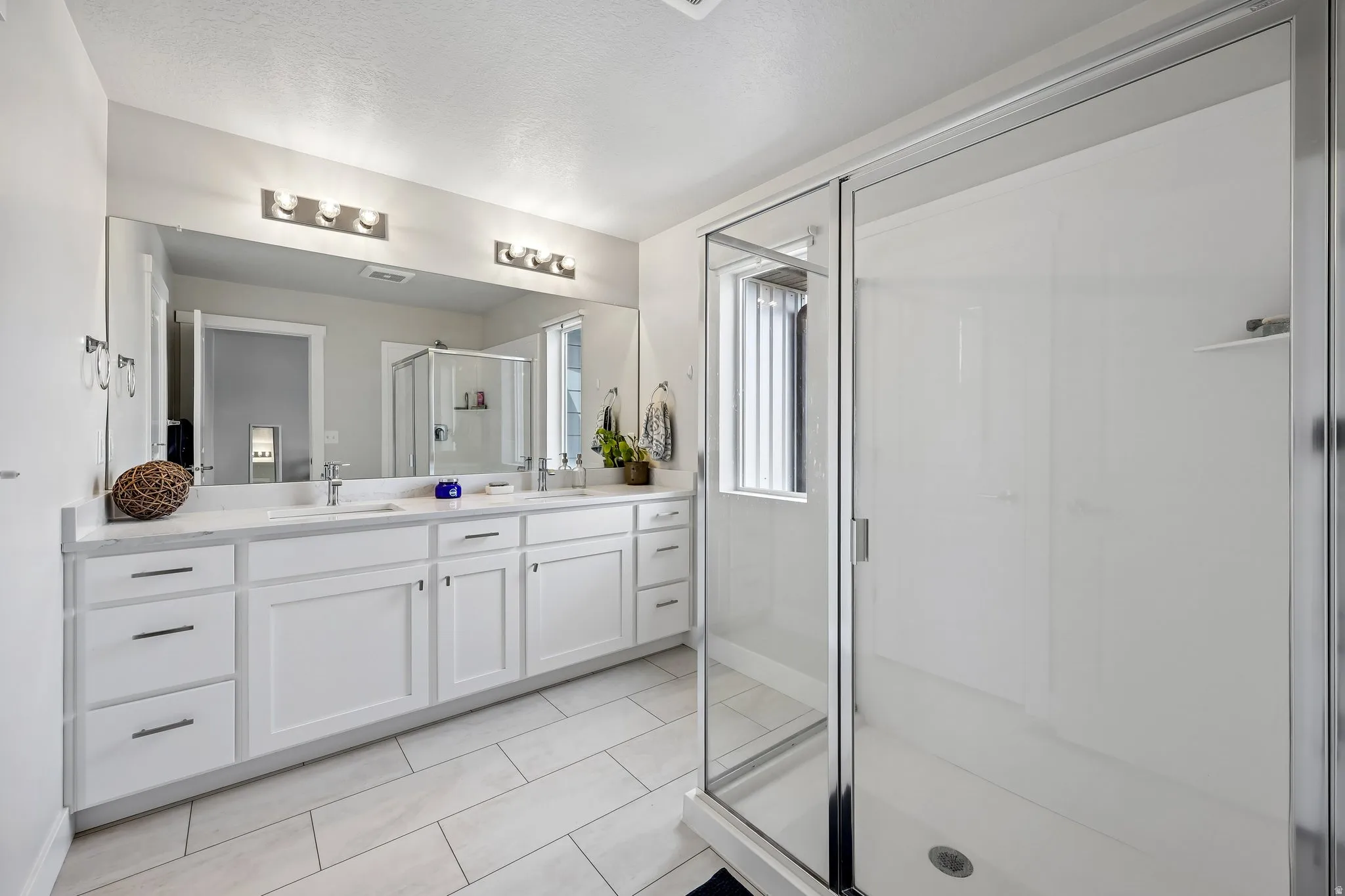 Full bath featuring a stall shower, double vanity, light tile patterned floors, and a textured ceiling