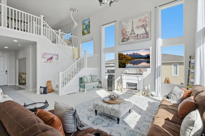 Two-story living area featuring a prominent staircase with white balusters and railings, multiple large windows, and a decorative fireplace with mantel