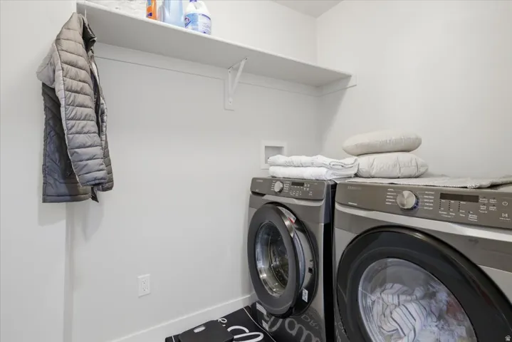 Dedicated laundry area featuring a white wall shelf, contemporary front-loading washer and dryer, and a built-in wall outlet