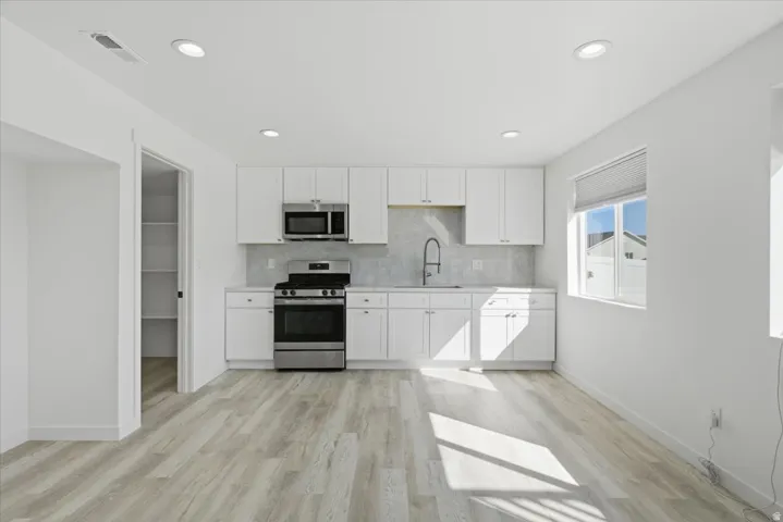 Contemporary kitchen featuring white cabinetry, stainless steel appliances, light-toned countertops, and a full-height backsplash