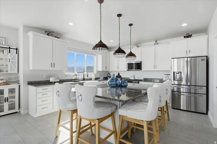 Contemporary kitchen featuring white cabinetry, grey granite countertops, stainless steel appliances, and a central island with pendant lighting