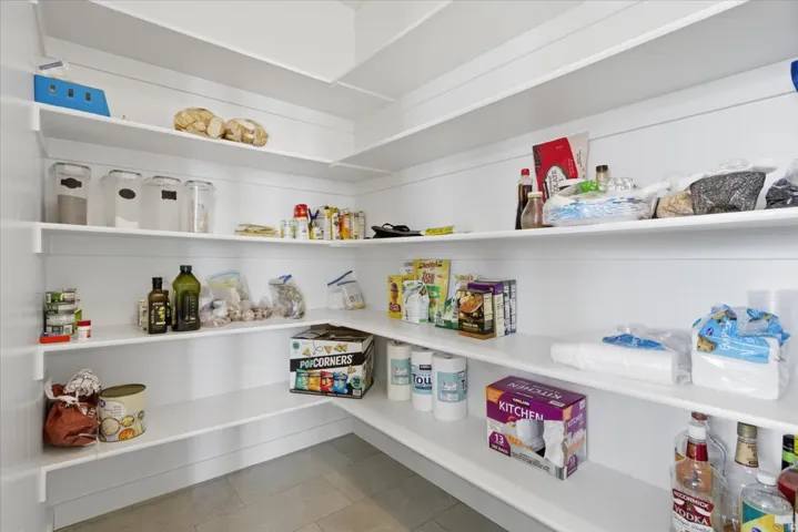 Expansive walk-in pantry featuring multiple levels of white shelving and light tile flooring