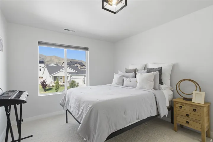 Light-colored carpeted room featuring a large window, white walls, and a black ceiling-mounted light fixture