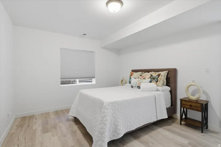 Bedroom featuring light wood-finish flooring, white walls, and a window with blinds