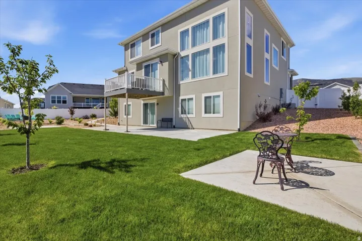 Expansive backyard featuring a large green lawn, concrete patio, and a second-story balcony with white railings