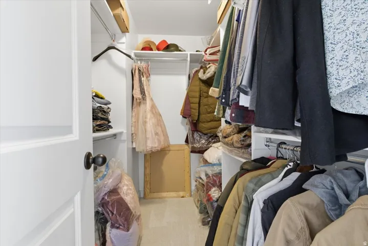 Walk-in closet featuring white shelving, multiple hanging rods, and light-colored carpeting
