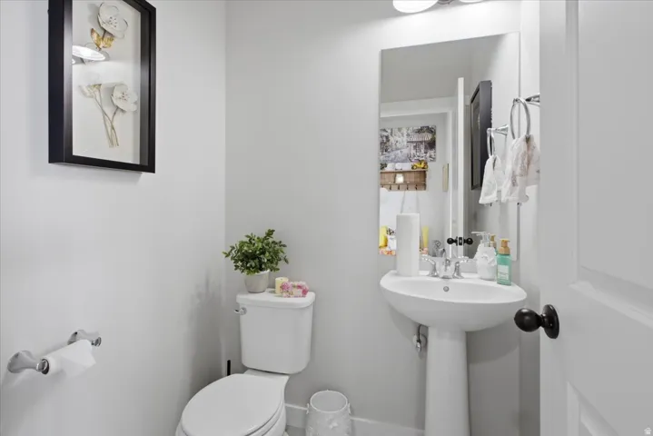 Pedestal sink with chrome faucet, wall-mounted mirror, and overhead vanity lighting