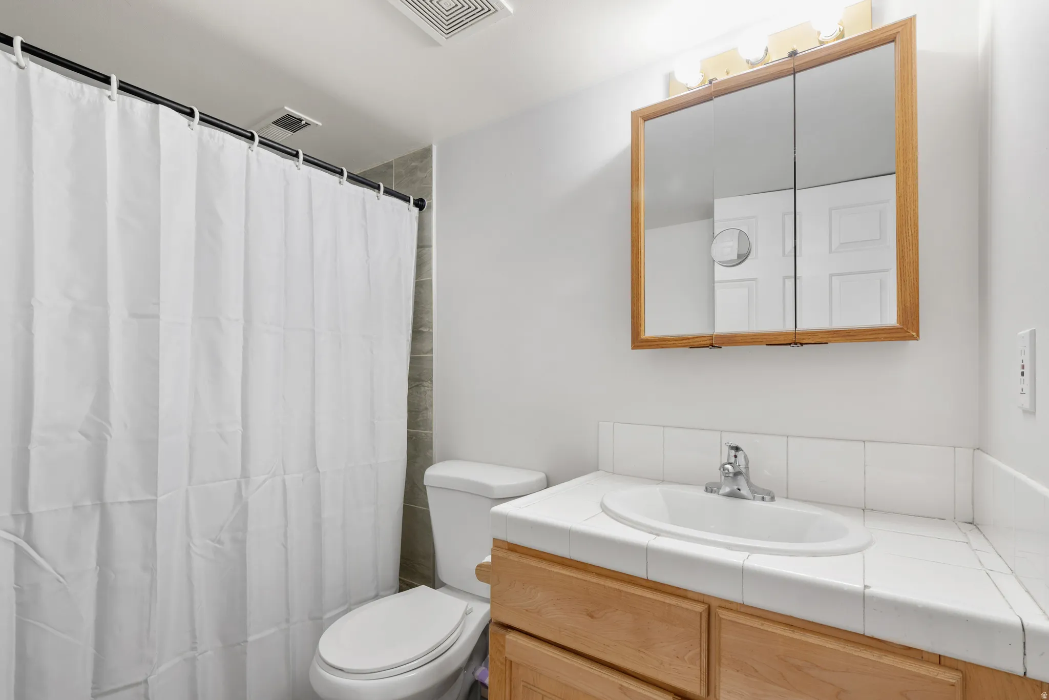 Bathroom featuring a wood-finish vanity with a tile countertop, integrated sink, and a mirrored medicine cabinet with wood framing