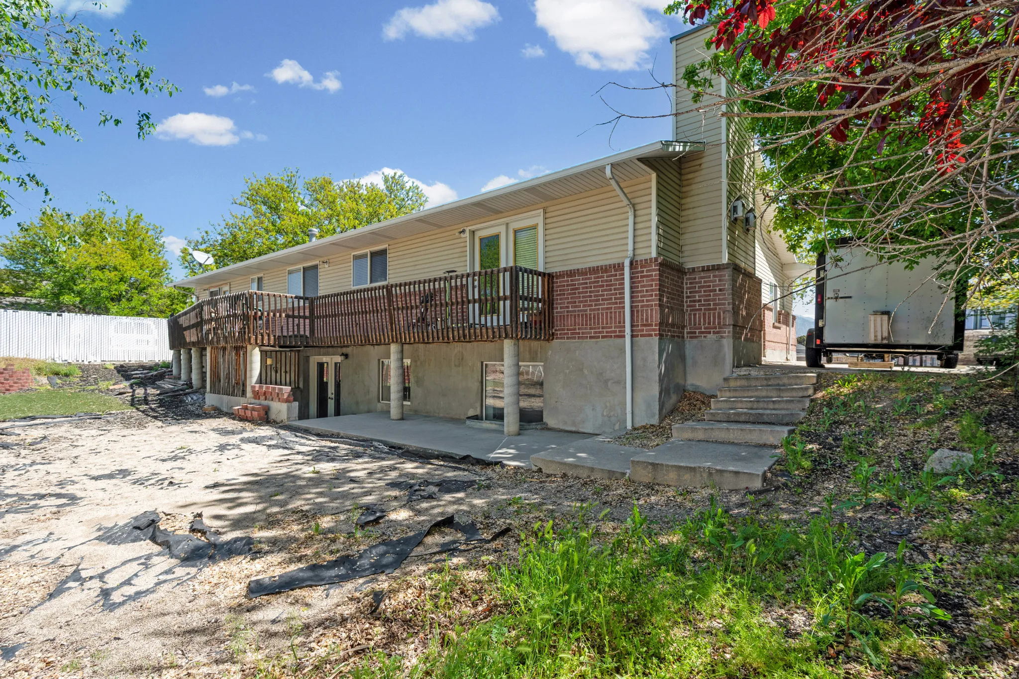 Multi-level exterior featuring tan siding, a brick facade, and a ground-level concrete patio