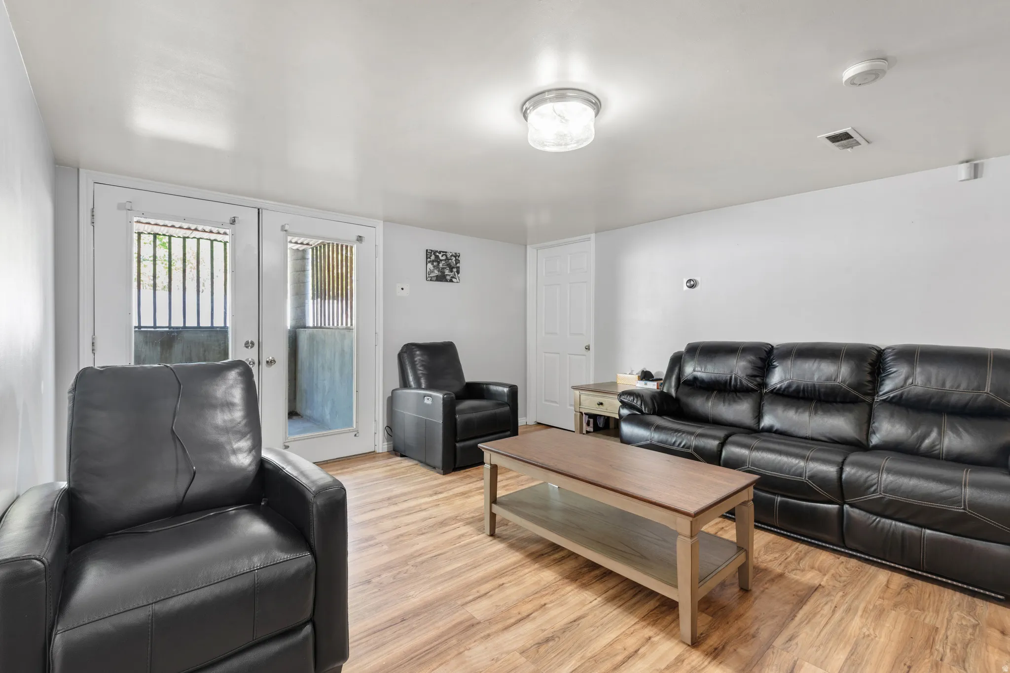 Spacious living area featuring wood-finish flooring, white walls, and a white ceiling with flush-mount lighting