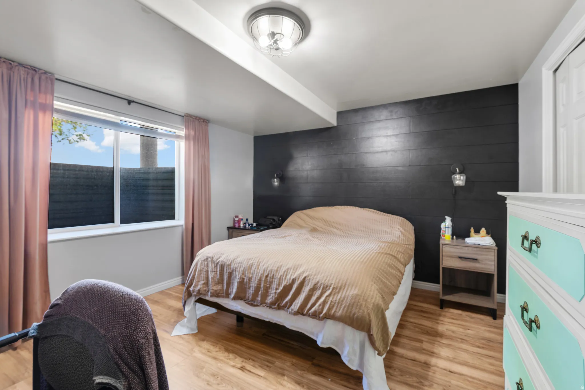 Bedroom featuring wood-finish flooring, a contemporary ceiling light fixture, and a window with roller shades