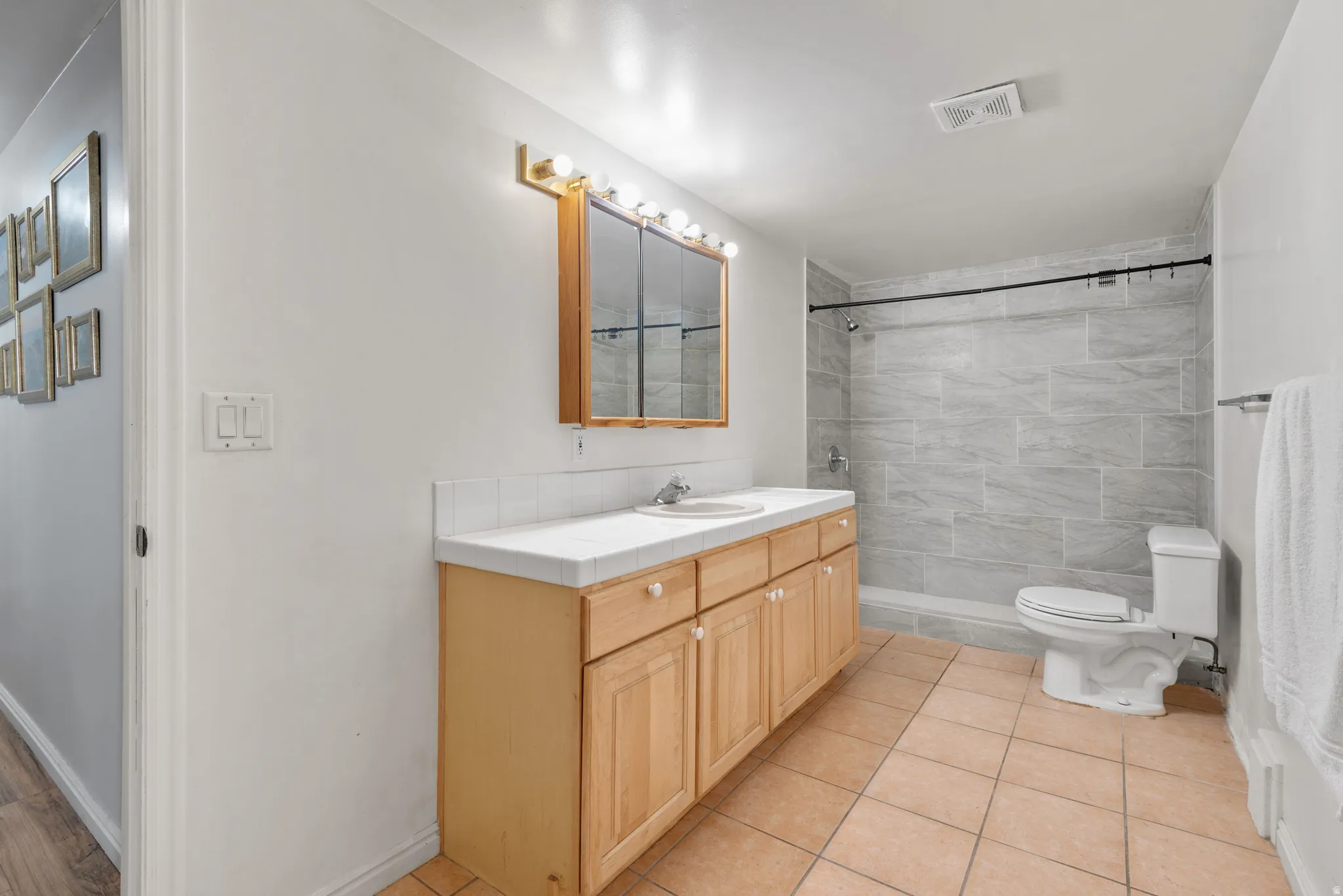 Spacious bathroom featuring a light wood-finish vanity with dual sinks, a white countertop, and a mirrored medicine cabinet