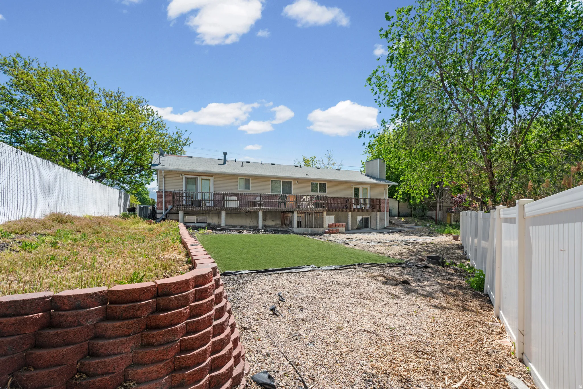 Expansive backyard featuring a retaining wall, artificial turf area, wood chip ground cover, and full privacy fencing