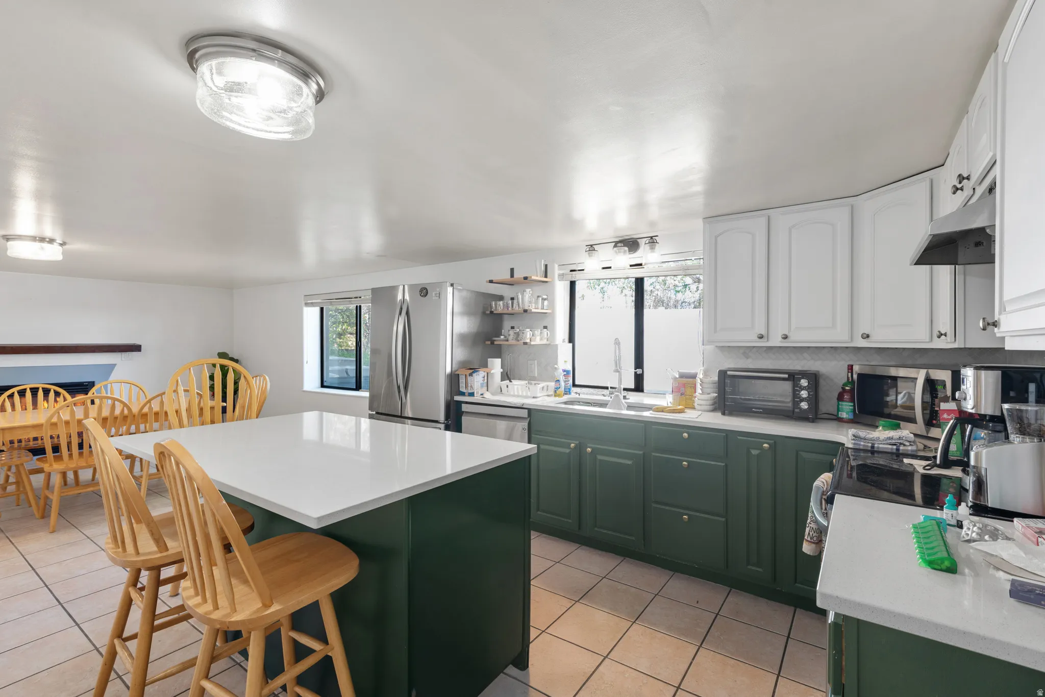 Kitchen featuring a central island with white countertop, contrasting green base cabinetry, white upper cabinetry, and stainless steel appliances